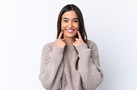 Dentist pointing to smile and holding model of dental implants in Buzzards Bay