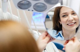 Woman admiring her teeth in mirror after teeth whitening treatment