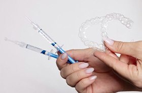 Hands holding custom whitening trays and syringes to fill the trays