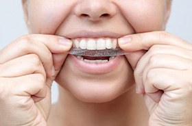 Woman placing whitening strip on her teeth