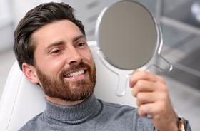 Dental patient holding mirror, admiring his new smile