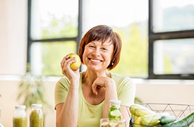 Woman with dental implants in Buzzards Bay holding an apple