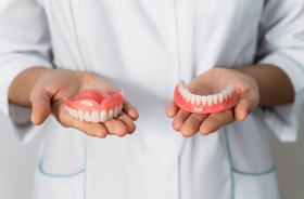 Person in white coat holding upper and lower dentures
