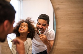 Father and daughter brushing teeth in front of bathroom mirror