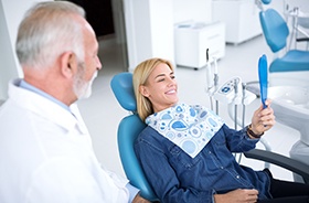 Patient looking at hand mirror with dentist