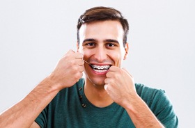 Young man with traditional braces using dental floss