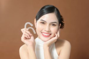 Happy young woman holding two Invisalign aligners