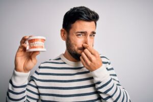 Man holding prosthetic teeth and pinching his nose 